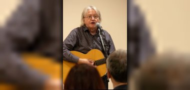 Manfred Pollmann mit Gitarre in der Hand singt in ein vor ihm stehendes Mikorfon