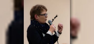 Dr. Tanja Machalet hält ein Mikro in der Hand und spricht, wobei sie mit der freien Hand gestikuliert.