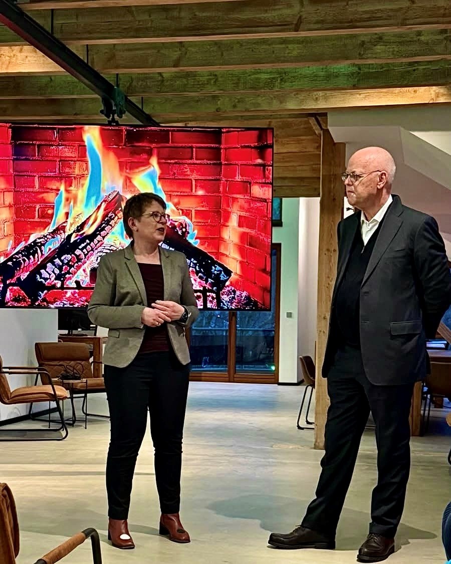 Dr. Tanja Machalet und Rudolph Scharping vor einer Leinwand, die ein brennendes Kaminfeuer zeigt