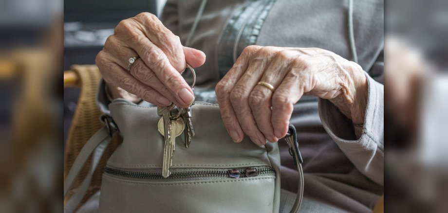 Hände einer Seniorin, die einen Bund mit Schlüsseln aus einer cremefarbenen Lederhandtasche nehmen