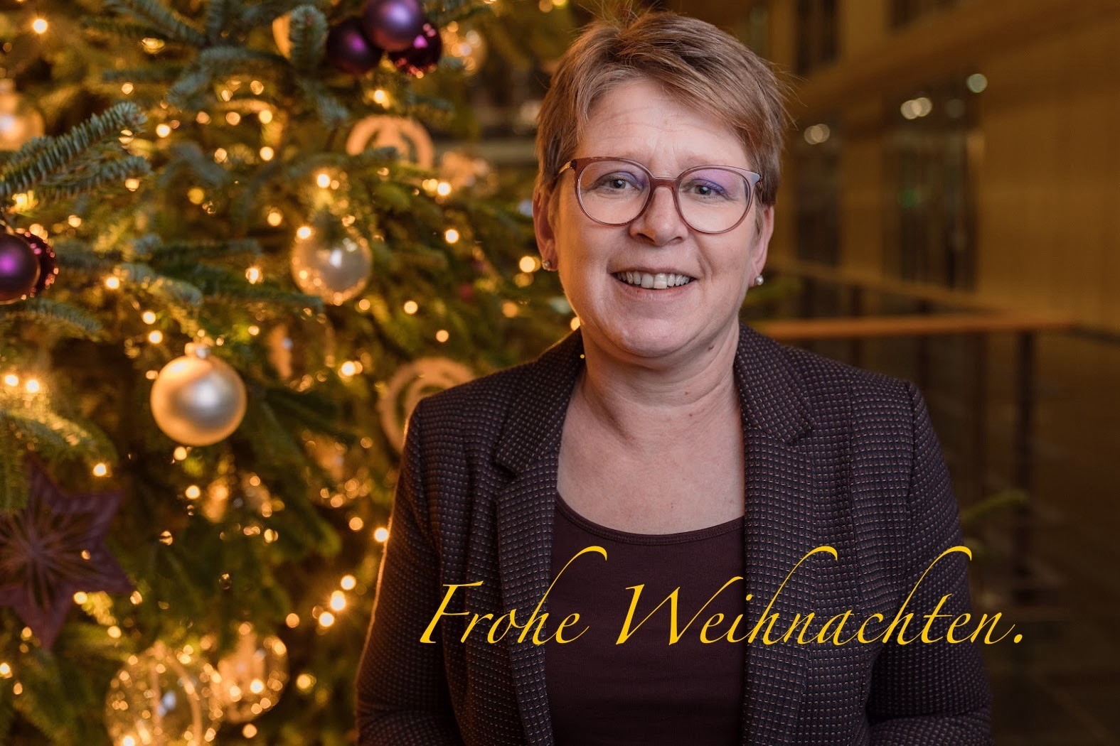 Tanja Machalet vor einem geschmückten Weihnachtsbaum, Kerzenlicht, am unteren Rand steht "Frohe Weihnachten"