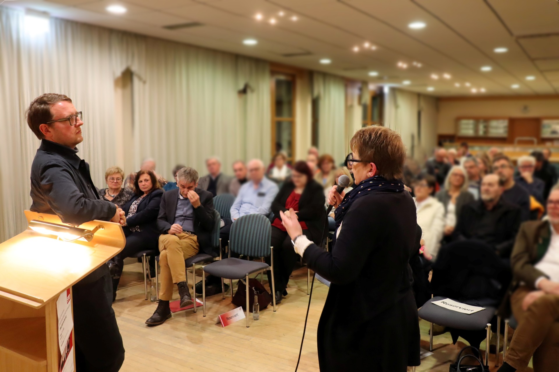 Dr. Tanja Machalet mit Mikro in der Hand, gestikulierend im Gespräch mit Prof. Dr. Quendt. Im Hintergrund vollbesetzter Zuschauerraum, u.a. in der ersten Reihe zu erkennen: Landtagspräsident (RLP), Hendrik Hering