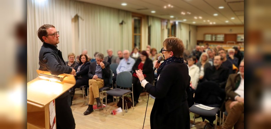 Dr. Tanja Machalet mit Mikro in der Hand, gestikulierend im Gespräch mit Prof. Dr. Quendt. Im Hintergrund vollbesetzter Zuschauerraum, u.a. in der ersten Reihe zu erkennen: Landtagspräsident (RLP), Hendrik Hering